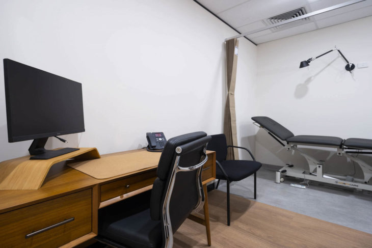 Medical Check-Up Room With A Monitor On A Wooden Table And A Physio Chair Next To The Wall