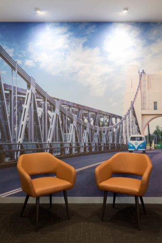 McCullough Centre - Distinctive urban styling in the treatment area featuring two brown chairs against a mural backdrop of a bridge, designed by Consilo, creating a refined and calming atmosphere