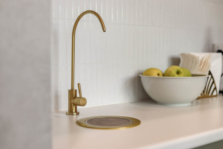 A Kitchen Sink with a Gold Faucet and Bowl of Apples