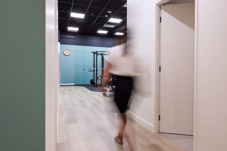 Refine Physiotherapy - Silhouette of a Woman Walking in a Well-Equipped Gym Room, with Dynamic Lighting and Modern Exercise Equipment.